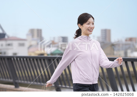 A middle-aged woman walking along the riverbank in sportswear. A middle-aged woman walking along the riverbank in sportswear. 142025008