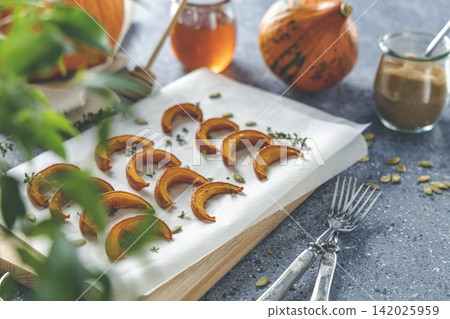 Autumn vegetarian food recipe. Baked mini pumpkin with herbs, and honey on a wooden board over grey table. Autumn vegetarian food recipe. Baked mini pumpkin with herbs, and honey on a wooden board over grey table. 142025959