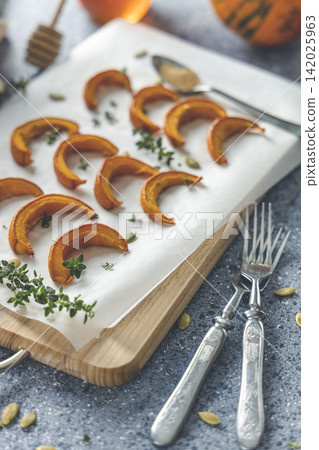 Autumn vegetarian food recipe. Baked mini pumpkin with herbs, and honey on a wooden board over grey table. Autumn vegetarian food recipe. Baked mini pumpkin with herbs, and honey on a wooden board over grey table. 142025963
