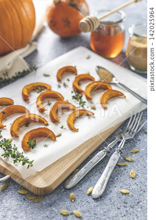 Baked mini pumpkin slices with thyme on a wooden board over grey table. Seasonal food vegetarian recipe. Baked mini pumpkin slices with thyme on a wooden board over grey table. Seasonal food vegetarian recipe. 142025964