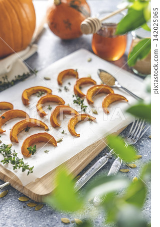 Baked mini pumpkin slices with thyme on a wooden board over grey table. Seasonal food vegetarian recipe. Baked mini pumpkin slices with thyme on a wooden board over grey table. Seasonal food vegetarian recipe. 142025965