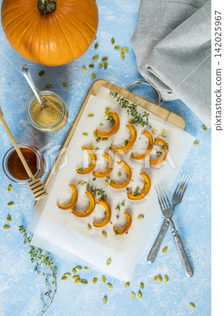 Autumn vegetarian food recipe. Baked mini pumpkin with herbs, and honey on a wooden board over light blue table top view. Autumn vegetarian food recipe. Baked mini pumpkin with herbs, and honey on a wooden board over light blue table top view. 142025967