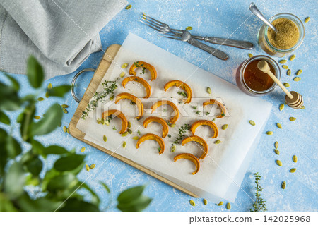 Autumn vegetarian food recipe. Baked mini pumpkin with herbs, and honey on a wooden board over light blue table top view. Autumn vegetarian food recipe. Baked mini pumpkin with herbs, and honey on a wooden board over light blue table top view. 142025968