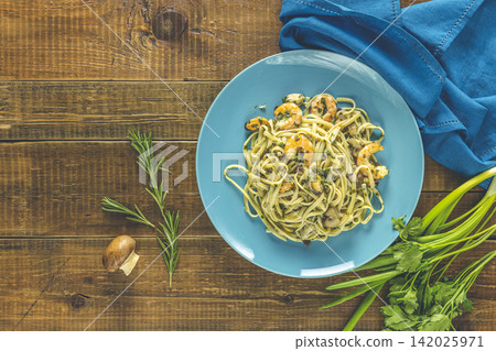 Pasta linguine with mushrooms, shrimps and seafood mussels, cheese and herbs, in blue ceramic plate on a dark wooden table surface Pasta linguine with mushrooms, shrimps and seafood mussels, cheese and herbs, in blue ceramic plate on a dark wooden table surface 142025971