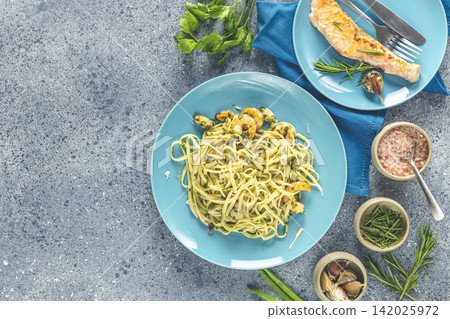 Pasta linguine with mushrooms, shrimps and seafood mussels, cheese and herbs, in blue ceramic plate on a light gray surface. Pasta linguine with mushrooms, shrimps and seafood mussels, cheese and herbs, in blue ceramic plate on a light gray surface. 142025972