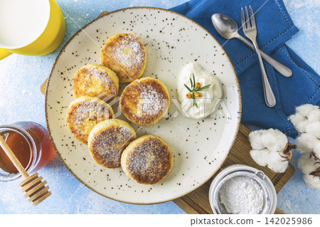 Cottage cheese pancakes, syrniki, ricotta fritters on ceramic plate. Gourmet healthy delicious morning breakfast. Flat lay, blue background. Cottage cheese pancakes, syrniki, ricotta fritters on ceramic plate. Gourmet healthy delicious morning breakfast. Flat lay, blue background. 142025986