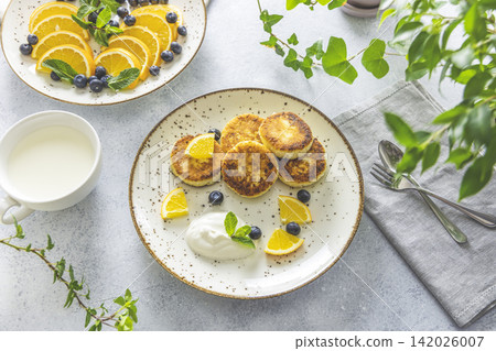 Delicious breakfast with curd fritter, ricotta fritter or cottage cheese pancakes on ceramic plate. Gourmet healthy delicious morning breakfast. Morning sunny time Delicious breakfast with curd fritter, ricotta fritter or cottage cheese pancakes on ceramic plate. Gourmet healthy delicious morning breakfast. Morning sunny time 142026007