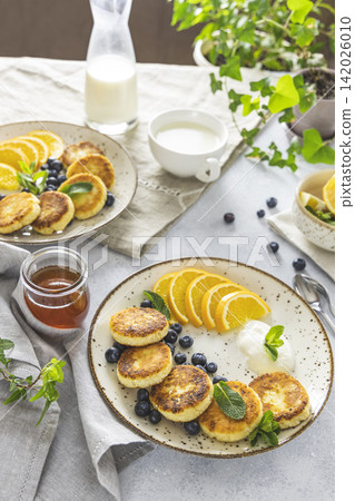 Delicious breakfast with curd fritter, ricotta fritter or cottage cheese pancakes on ceramic plate. Gourmet healthy delicious morning breakfast. Morning sunny time Delicious breakfast with curd fritter, ricotta fritter or cottage cheese pancakes on ceramic plate. Gourmet healthy delicious morning breakfast. Morning sunny time 142026010