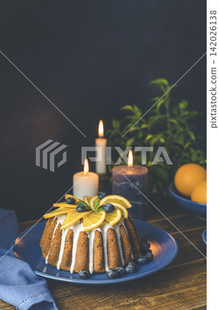 Orange bundt cake with blueberry surrounded fruits, candles, plant and cutleries on dark wooden background. Orange bundt cake with blueberry surrounded fruits, candles, plant and cutleries on dark wooden background. 142026138