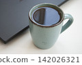 cup of black tea on the table next to the laptop 142026321