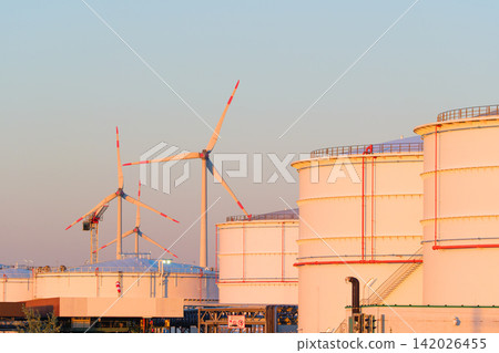 Large oil storage tanks at an industrial refinery facility with wind turbines in the background. Large oil storage tanks at an industrial refinery facility with wind turbines in the background. 142026455