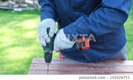 Worker man working with Screwdriver. Person using a red cordless drill with a metal spiral drill bit in a workshop, construction, diy project task. Accu battery hand drill. Screwing a screw assembling 142026751