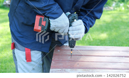 Worker man working with Screwdriver. Person using a red cordless drill with a metal spiral drill bit in a workshop, construction, diy project task. Accu battery hand drill. Screwing a screw assembling Worker man working with Screwdriver. Person using a red cordless drill with a metal spiral drill bit in a workshop, construction, diy project task. Accu battery hand drill. Screwing a screw assembling 142026752