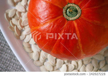Top view of whole ripe orange pumpkin and seeds on white plate Top view of whole ripe orange pumpkin and seeds on white plate 142027228