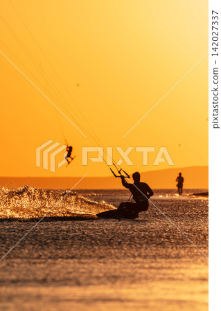 Kiter riding on sea water with warm golden sunset light Kiter riding on sea water with warm golden sunset light 142027337