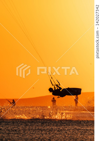 Kite surfer performing an aerial trick above the water at golden sunset Kite surfer performing an aerial trick above the water at golden sunset 142027342