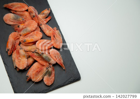 On a black stone tile (slate) on a white background lies a handful of frozen orange-pink shrimp covered with a thin layer of frost. Concept: marine ingredient, frozen and raw seafood. High quality On a black stone tile (slate) on a white background lies a handful of frozen orange-pink shrimp covered with a thin layer of frost. Concept: marine ingredient, frozen and raw seafood. High quality 142027799