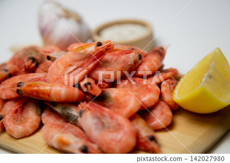 A close-up side view of frozen shrimps on a wooden board, two lemon slices diagonally, a salt shaker and a head of garlic next to it. Concept: an expanded set of seafood seasonings. High quality photo A close-up side view of frozen shrimps on a wooden board, two lemon slices diagonally, a salt shaker and a head of garlic next to it. Concept: an expanded set of seafood seasonings. High quality photo 142027980