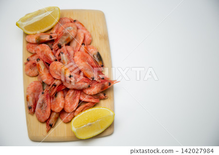 Top view of a light wooden cutting board with frozen shrimp in the center and two lemon slices diagonally. Concept: concise seafood serving. High quality photo Top view of a light wooden cutting board with frozen shrimp in the center and two lemon slices diagonally. Concept: concise seafood serving. High quality photo 142027984