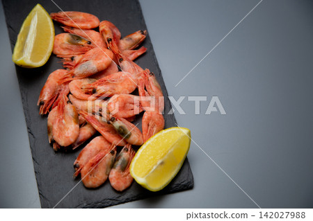 Top view of a black slate with frozen shrimps, on both sides of the composition there is one slice of lemon. Concept: symmetrical seafood framing, laconic serving. High quality photo Top view of a black slate with frozen shrimps, on both sides of the composition there is one slice of lemon. Concept: symmetrical seafood framing, laconic serving. High quality photo 142027988