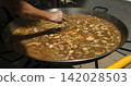 Chef checks large pan of chicken and green beans broth for Spanish paella during outdoor cooking event 142028503