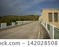 View along the top pathway of Beniarres Dam surrounded by green hills and clouds 142028508