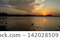 Scenic panorama of a sea view during sunset with clouds and a city silhouette in the background 142028509