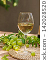 Glass of White Wine with Grapes and Leaves on Table 142028520