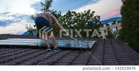 Man Washing Photovoltaic Panels on Sloped Residential Roof Man Washing Photovoltaic Panels on Sloped Residential Roof 142029076