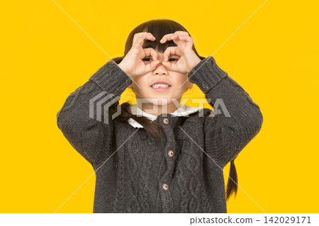 A playful elementary school girl looking through finger circles over her eyes like glasses or binoculars with a toothy grin A playful elementary school girl looking through finger circles over her eyes like glasses or binoculars with a toothy grin 142029171