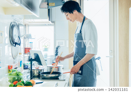 A young man cooking while looking at a tablet. A young man cooking while looking at a tablet. 142031181