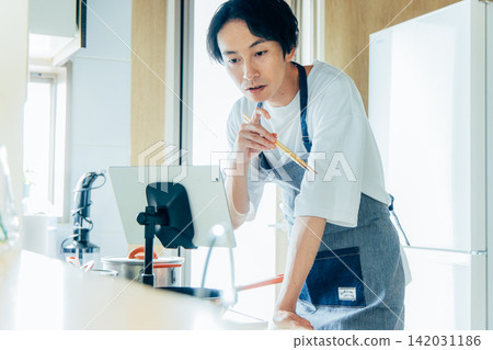 一位年輕男子一邊煮飯一邊看平板電腦。 142031186