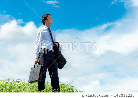A young man in a suit stands against a blue sky. A young man in a suit stands against a blue sky. 142031225
