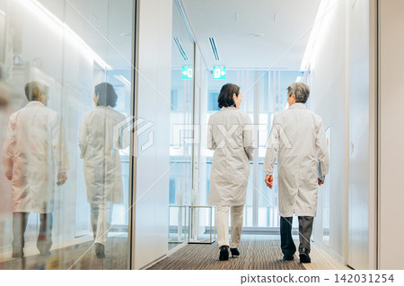 兩名五十多歲的研究人員身穿白色實驗服,走過一座研究設施。 兩名五十多歲的研究人員身穿白色實驗服,走過一座研究設施。 142031254