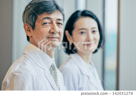 A male and female researcher in white coats gazing out the window of a research facility. A male and female researcher in white coats gazing out the window of a research facility. 142031279