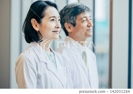 A male and female researcher in white coats gazing out the window of a research facility. A male and female researcher in white coats gazing out the window of a research facility. 142031284