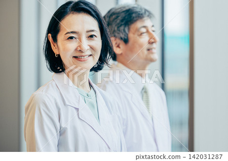 A male and female researcher in white coats gazing out the window of a research facility. A male and female researcher in white coats gazing out the window of a research facility. 142031287