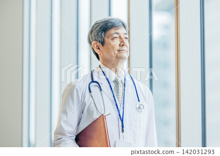 A portrait of a male doctor in his 60s wearing a white coat. A portrait of a male doctor in his 60s wearing a white coat. 142031293