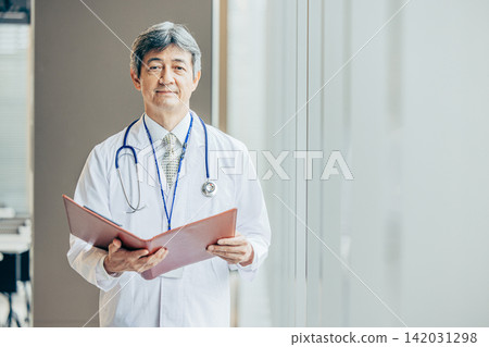 A portrait of a male doctor in his 60s wearing a white coat. A portrait of a male doctor in his 60s wearing a white coat. 142031298