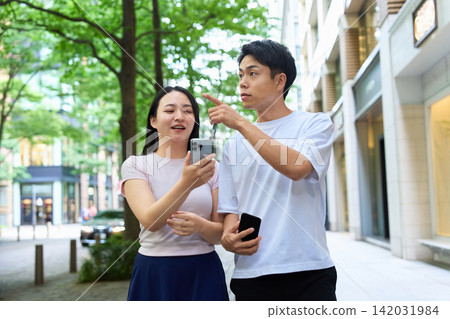 年輕男女手持智慧型手機走在城市裡。 年輕男女手持智慧型手機走在城市裡。 142031984