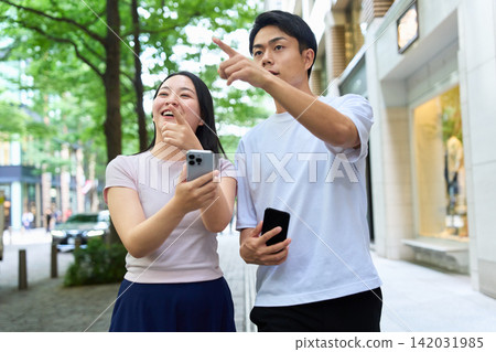年輕男女手持智慧型手機走在城市裡。 年輕男女手持智慧型手機走在城市裡。 142031985
