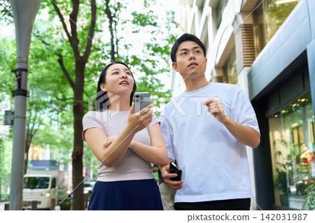 年輕男女手持智慧型手機走在城市裡。 年輕男女手持智慧型手機走在城市裡。 142031987