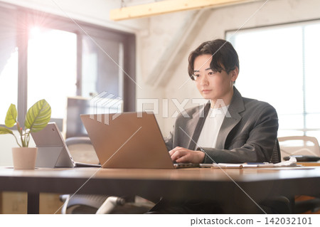 一位年輕的男性上班族在燈光明亮的辦公室裡使用筆記型電腦。 一位年輕的男性上班族在燈光明亮的辦公室裡使用筆記型電腦。 142032101