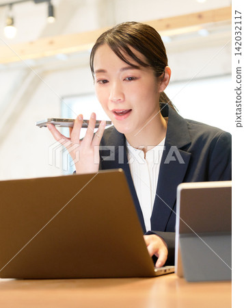 一位女商人透過對著智慧型手機說話來使用語音輸入。 142032117