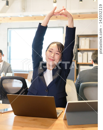 A female employee stretches during a break from working on her computer. A female employee stretches during a break from working on her computer. 142032119