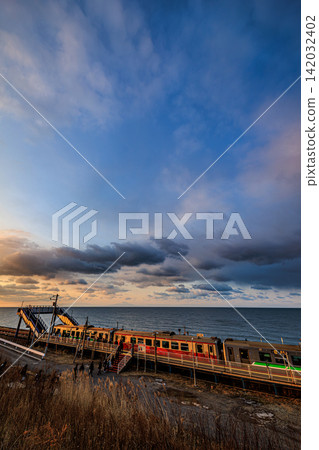 The train arriving at the station platform, facing the sea and a sky filled with the glow of dawn clouds, presents a truly evocative and romantic scene. The train arriving at the station platform, facing the sea and a sky filled with the glow of dawn clouds, presents a truly evocative and romantic scene. 142032402