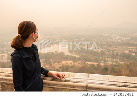 Asian woman looking to her town covered with PM2.5 pollution. PM2.5 levels meaning the air quality posed a health hazard. Asian woman looking to her town covered with PM2.5 pollution. PM2.5 levels meaning the air quality posed a health hazard. 142032491
