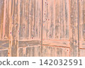 Orange-tinted old wooden door with wood grain texture and nail holes. 142032591