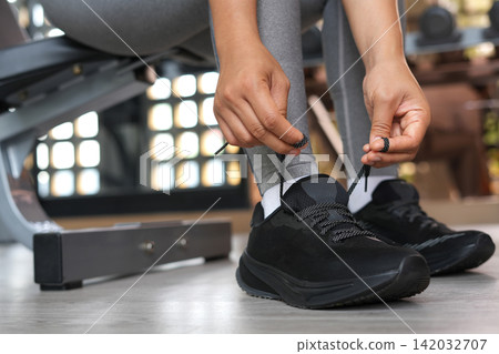 A woman ties her shoelaces ready to run at the gym. A woman ties her shoelaces ready to run at the gym. 142032707