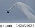 A jet plane flying through the blue sky, leaving a curved trail of white smoke. 142034024